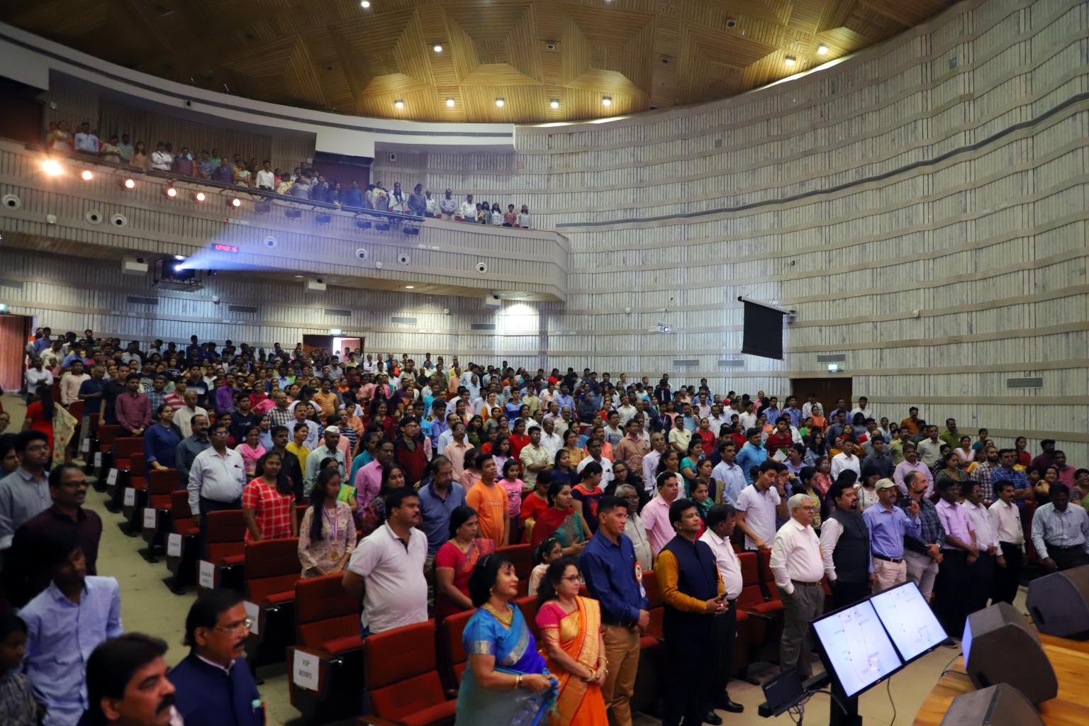 Avinash Chate addressing a large audience in an auditorium, with many attendees standing.